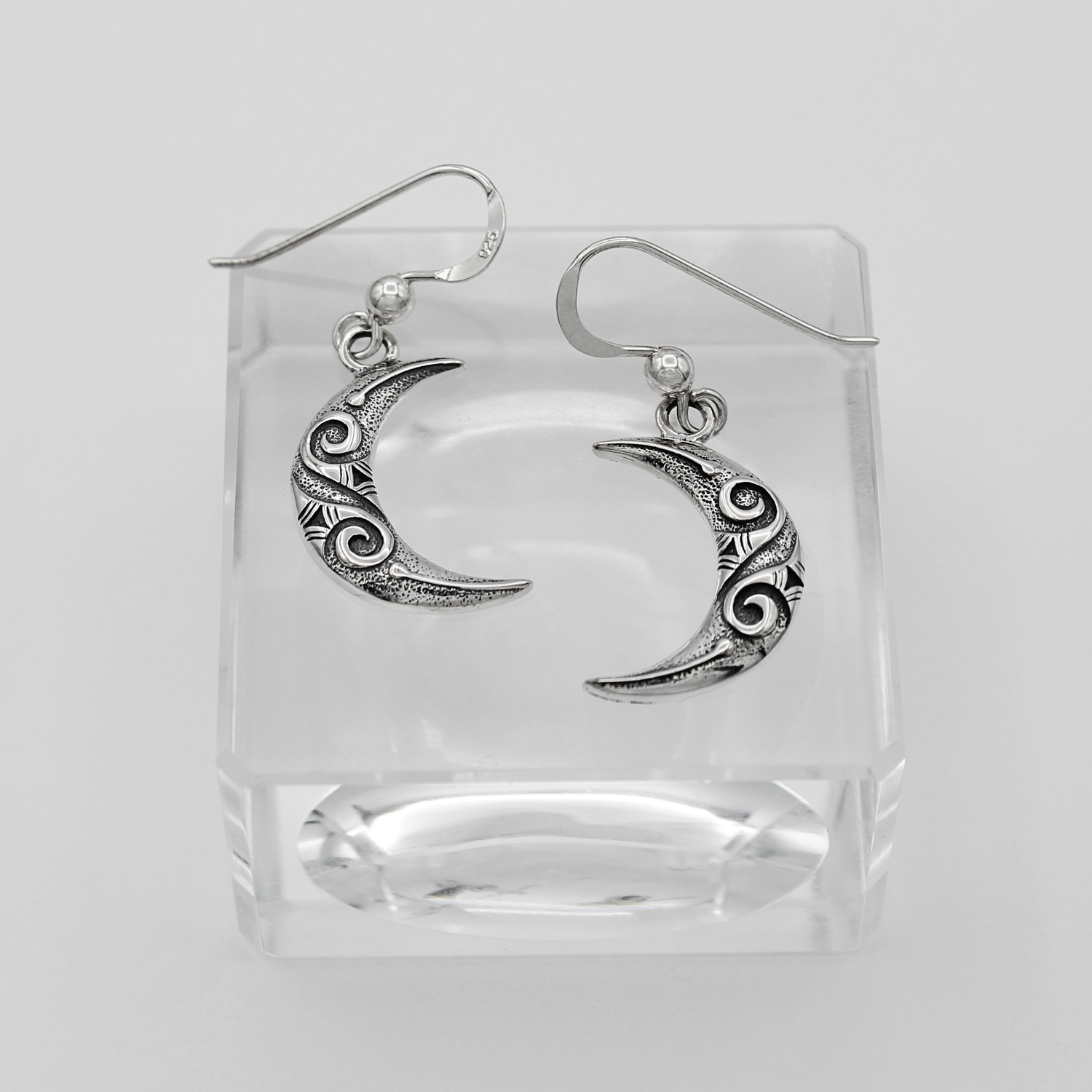 Silver hook earrings shaped like crescent moons with decorative swirl patterns on the surface
