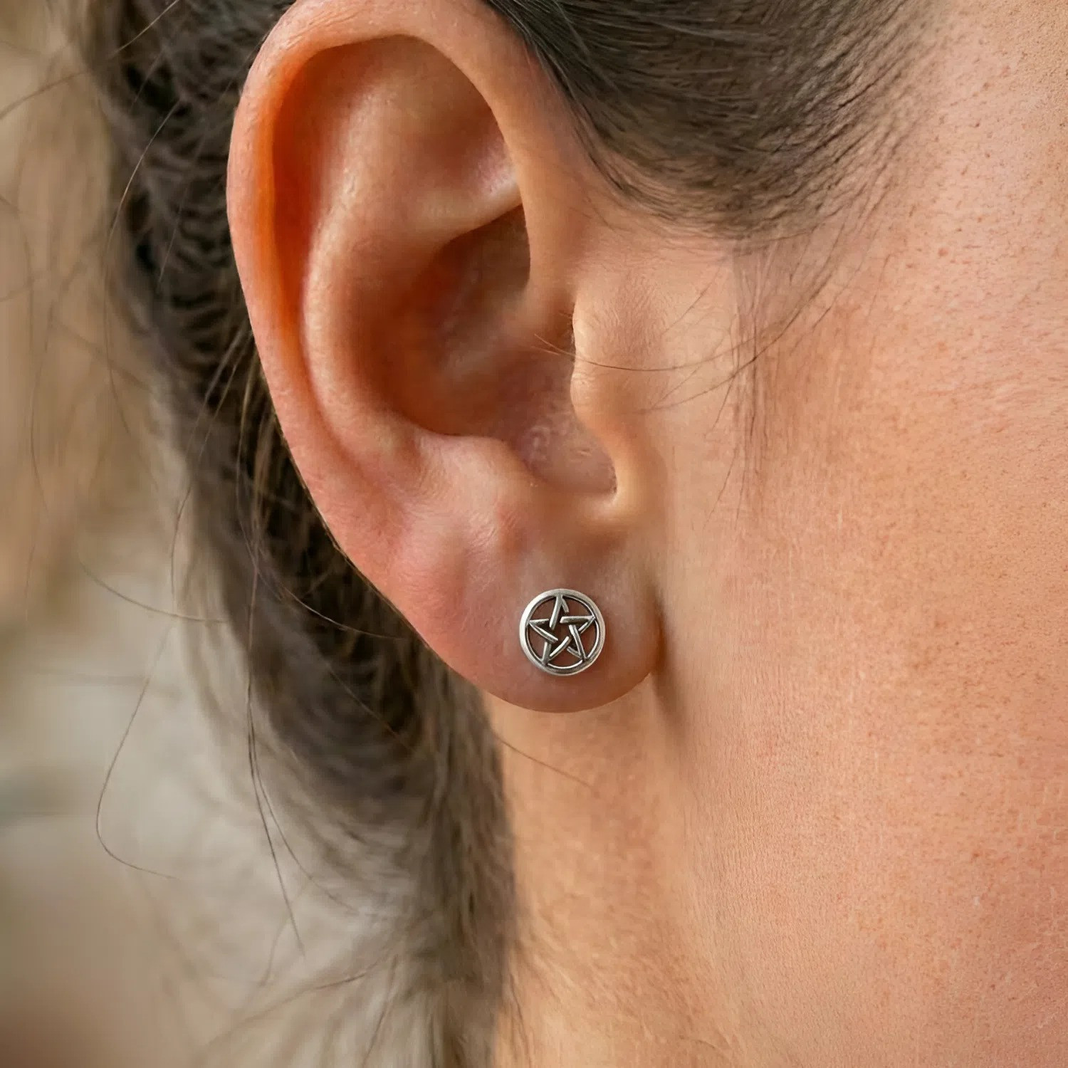 Tiny pentacle earrings in sterling silver, featuring a delicate minimalist pentagram design worn comfortably on a model's earlobe