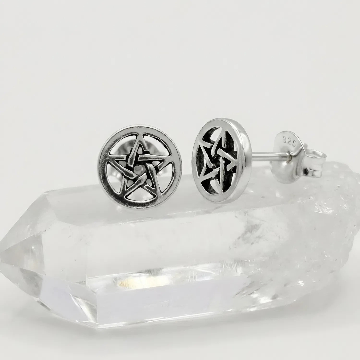 Silver pentacle earrings highlighting a tiny pentagram stud design, beautifully displayed resting on a natural clear quartz crystal point