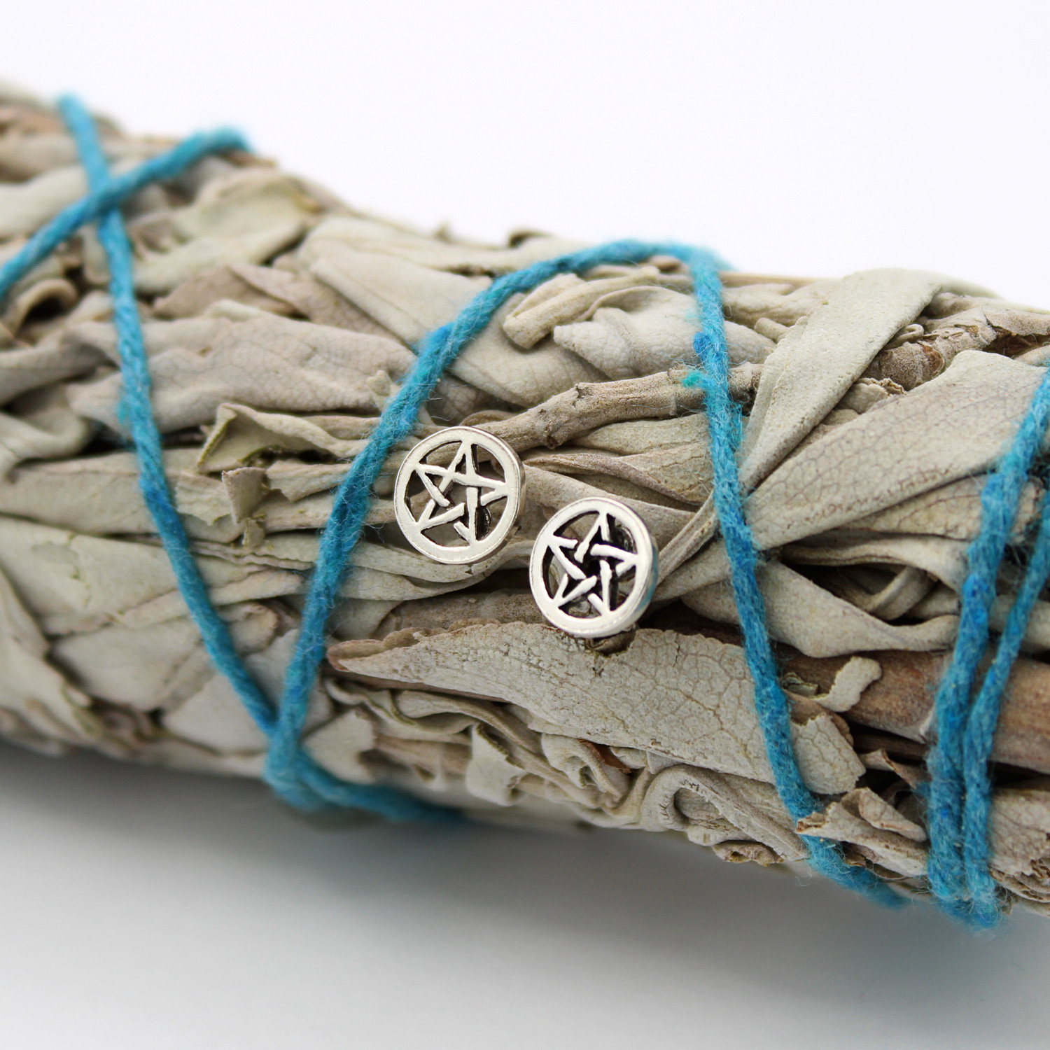 Pentacle studs crafted from sterling silver, tiny silver pentacle earrings resting elegantly on a bundle of dried sage tied with blue string