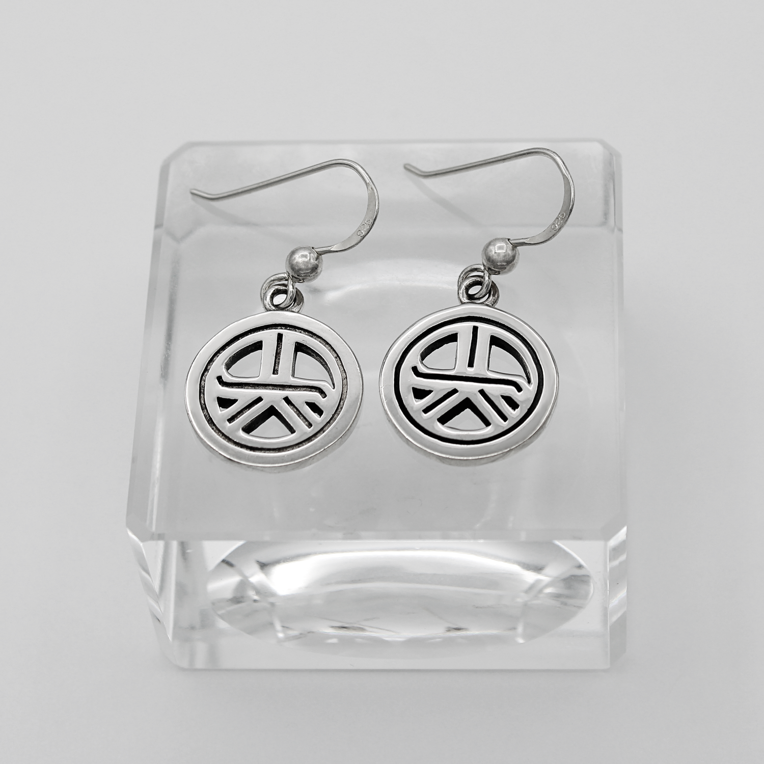 Silver hook earrings featuring a circular charm oxidized with the Tam A Ra Sha symbol
