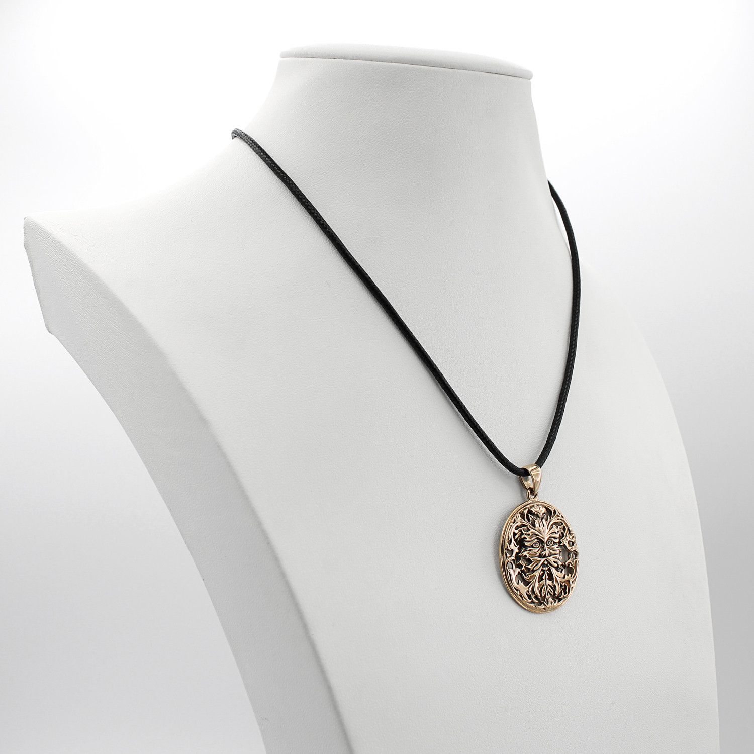 Greenman necklace displayed on a white jewelry bust, demonstrating the hanging scale and the black cord of this bronze pagan pendant