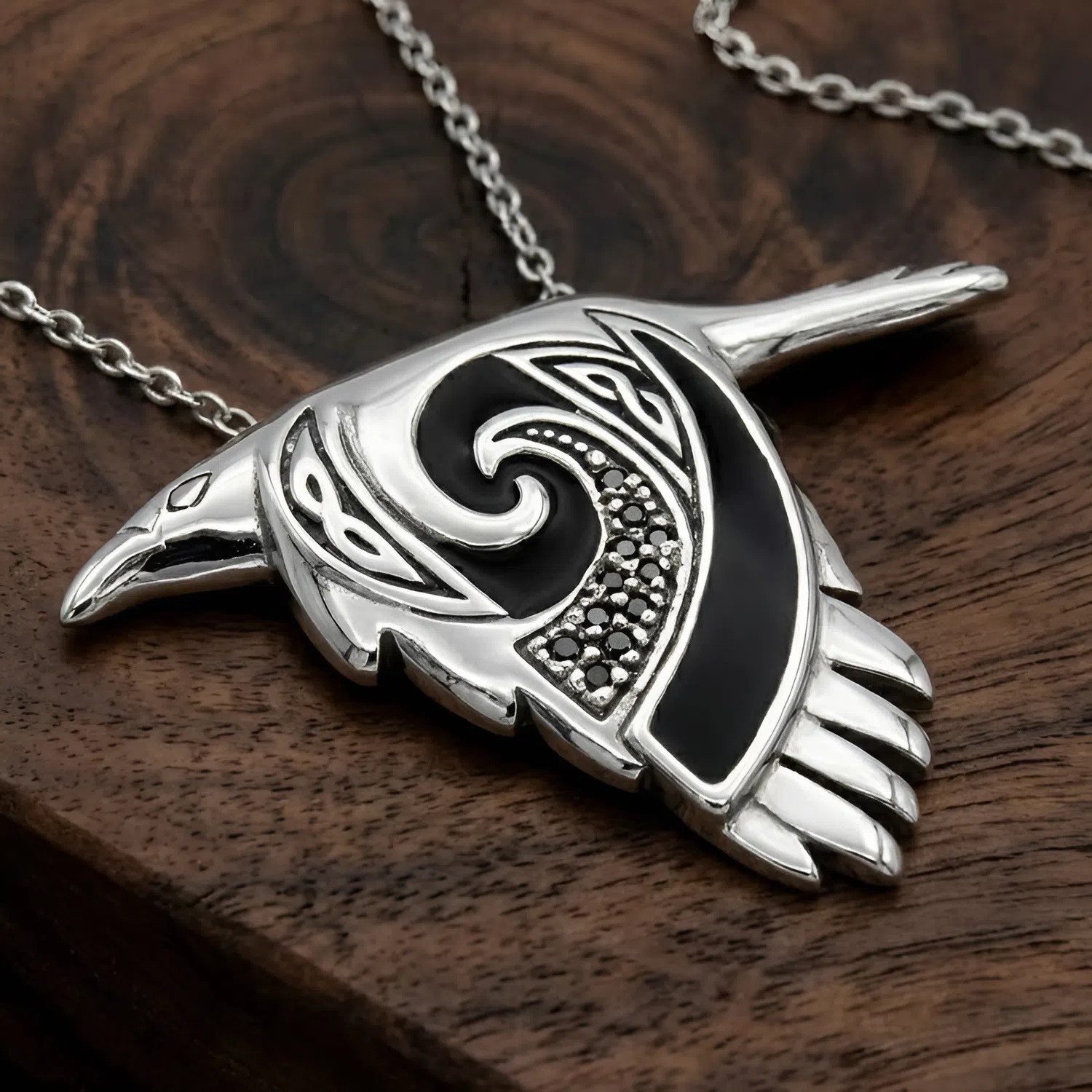 Witch familiar crow pendant in sterling silver at our pagan jewelry store, displaying an intricate Celtic spirit animal design resting on a dark wood grain surface