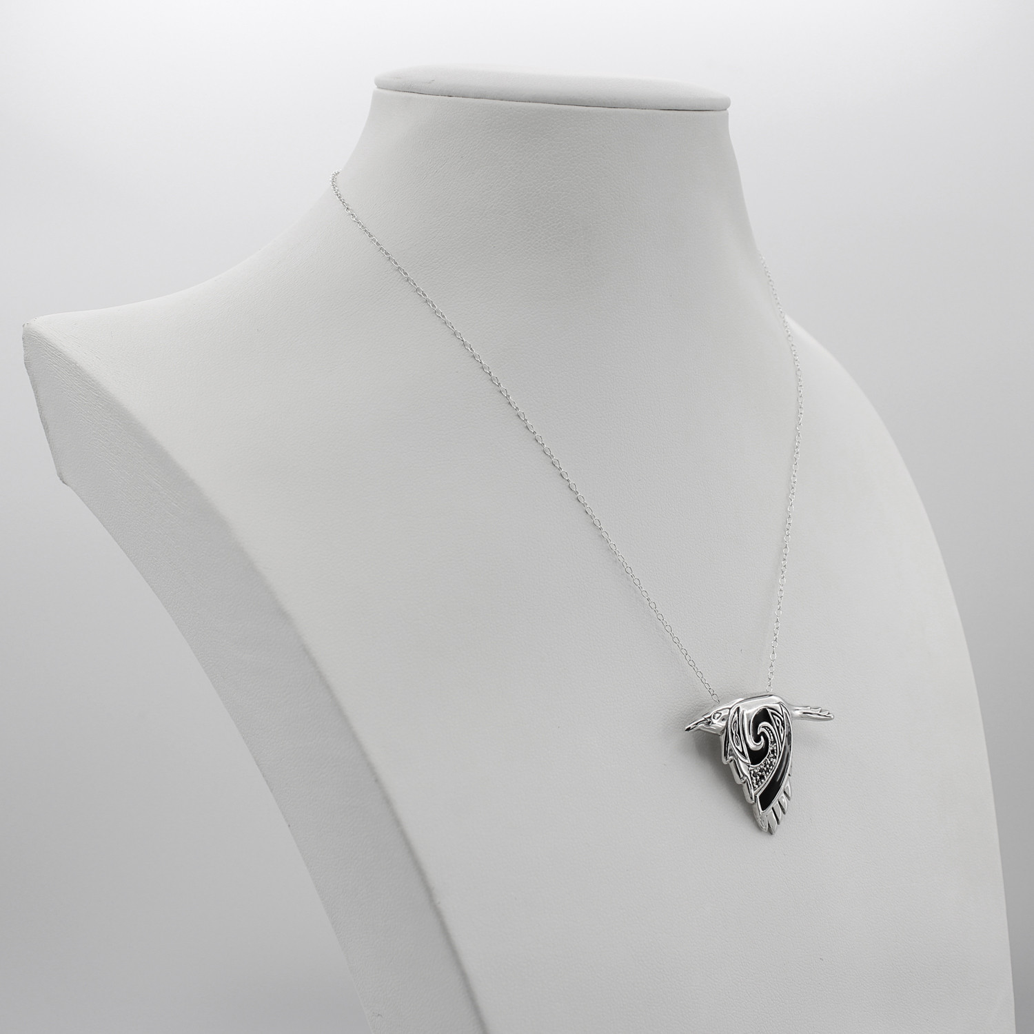 Sterling silver crow spirit animal necklace shown on a white jewelry display bust, highlighting the Celtic familiar design and chain length
