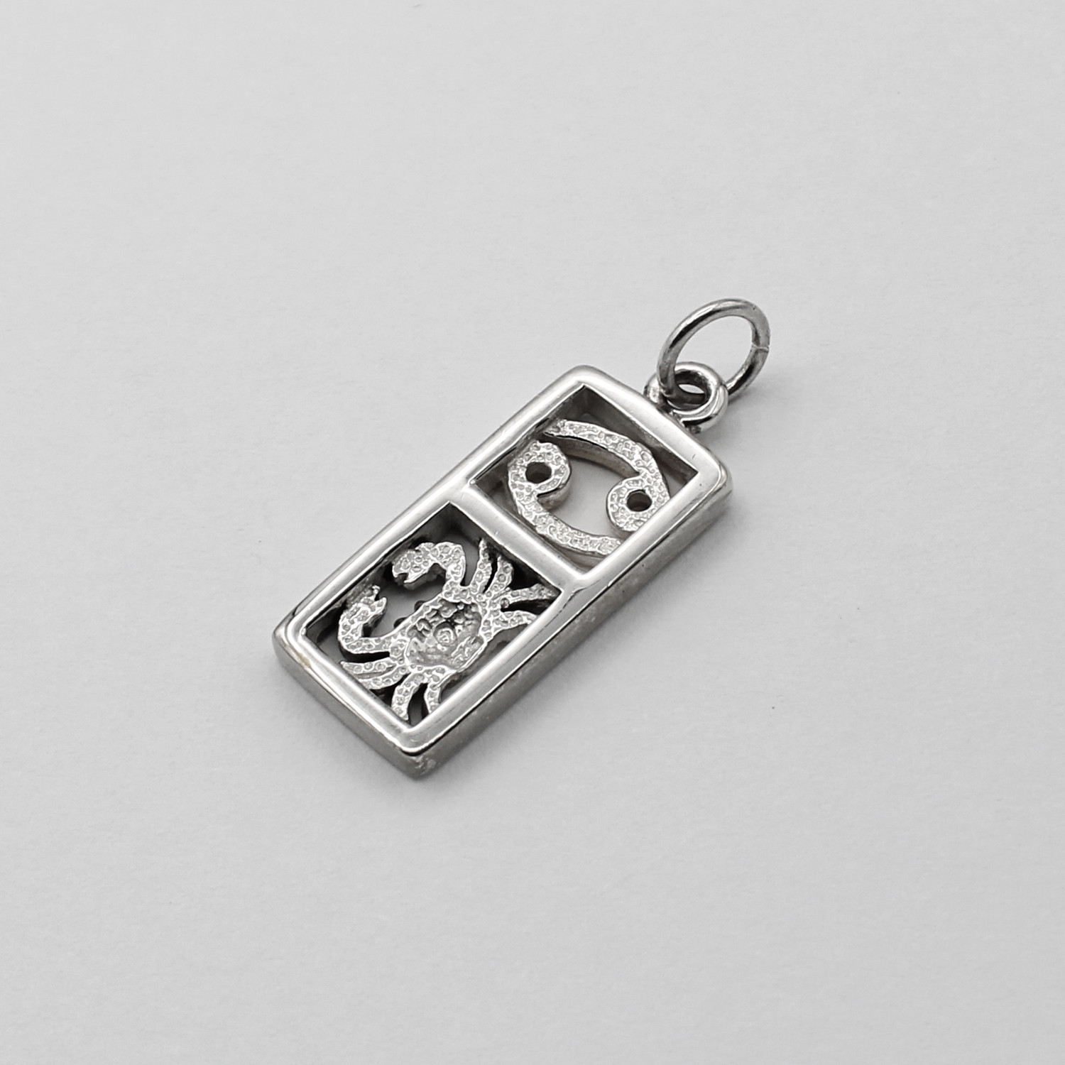 Angled flat lay of a Cancer horoscope charm on a crisp white background, emphasizing the textured back of the Zodiac sign pendant