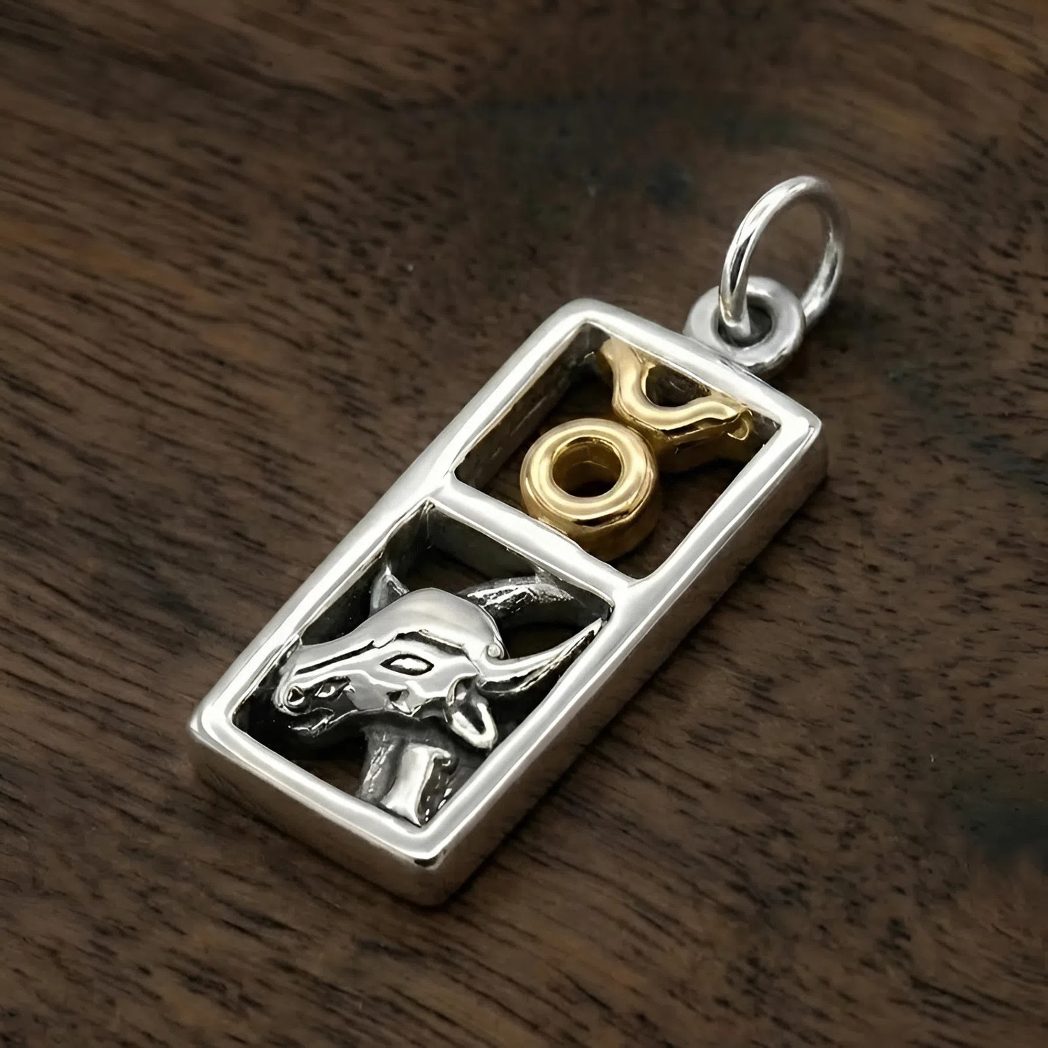 Close-up of a Taurus zodiac pendant resting on a dark wood surface at our witchcraft supply store, showcasing the high-polish silver and gold accents