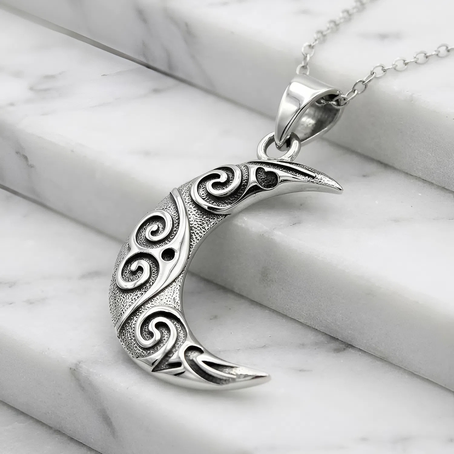 Oxidized sterling silver moon pendant resting gracefully on white marble steps, an elegant stylized moon necklace shaped like a textured crescent moon