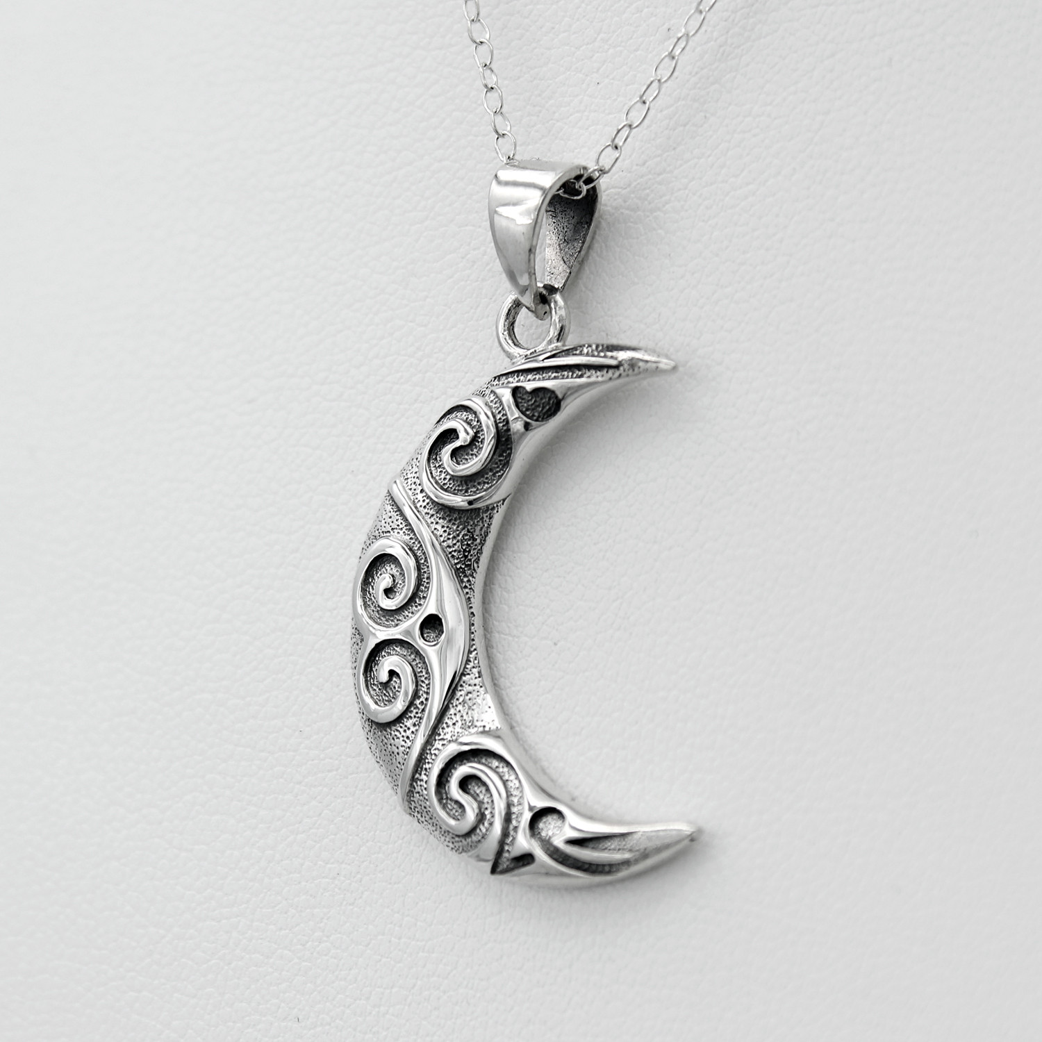 Oxidized moon necklace and stylized moon necklace captured from a close right angle, emphasizing the polished raised swirls on this crescent moon