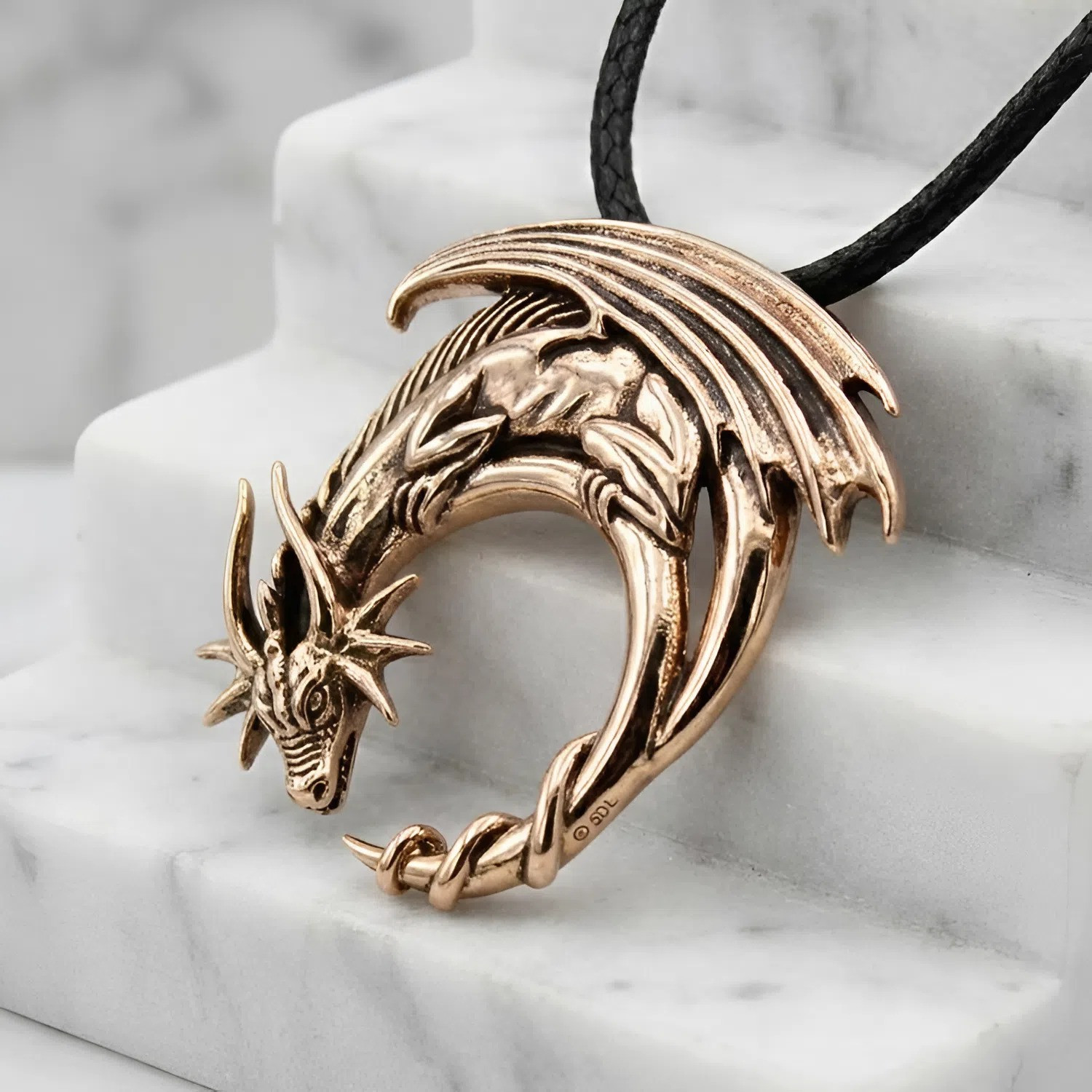 Dragon on moon pendant elegantly draped across white marble steps, emphasizing the glowing, highly reflective finish of this dragon jewelry piece