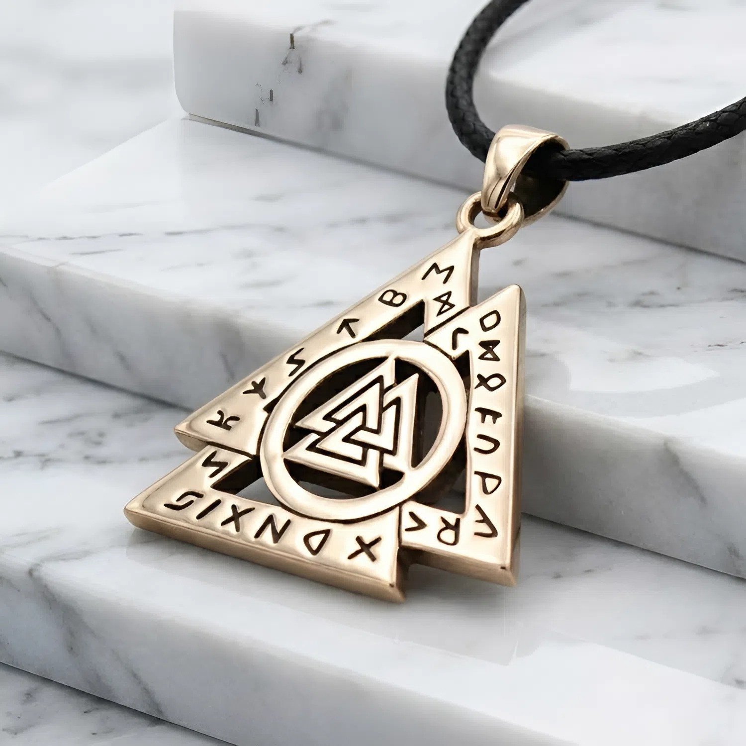Valknut with runes crafted in gold-colored bronze, elegantly draped across bright white marble steps to highlight the pagan jewelry details