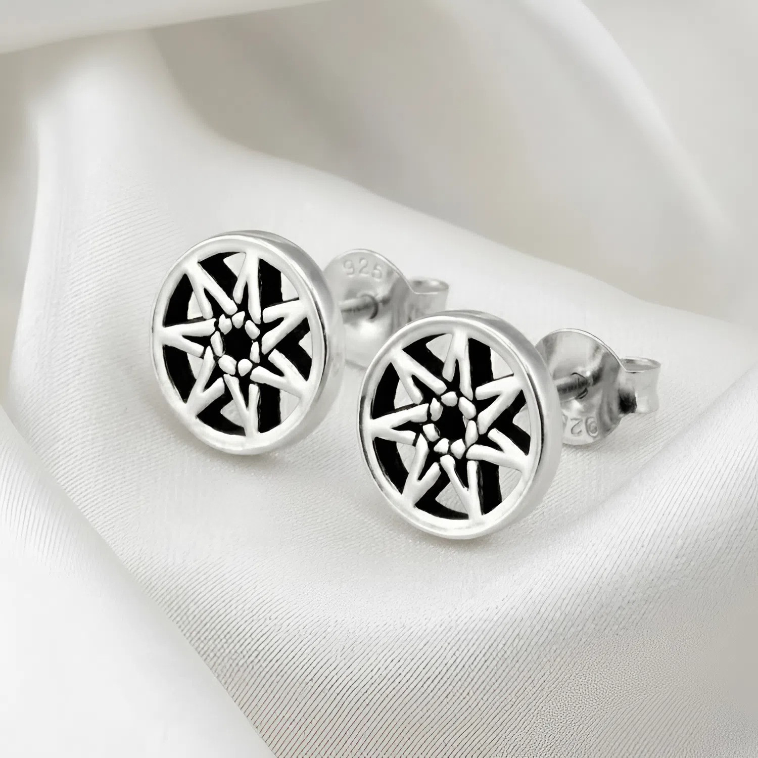 Faery star studs capturing a sleek, woven seven-pointed aesthetic, displayed gracefully on folded, smooth white silk fabric