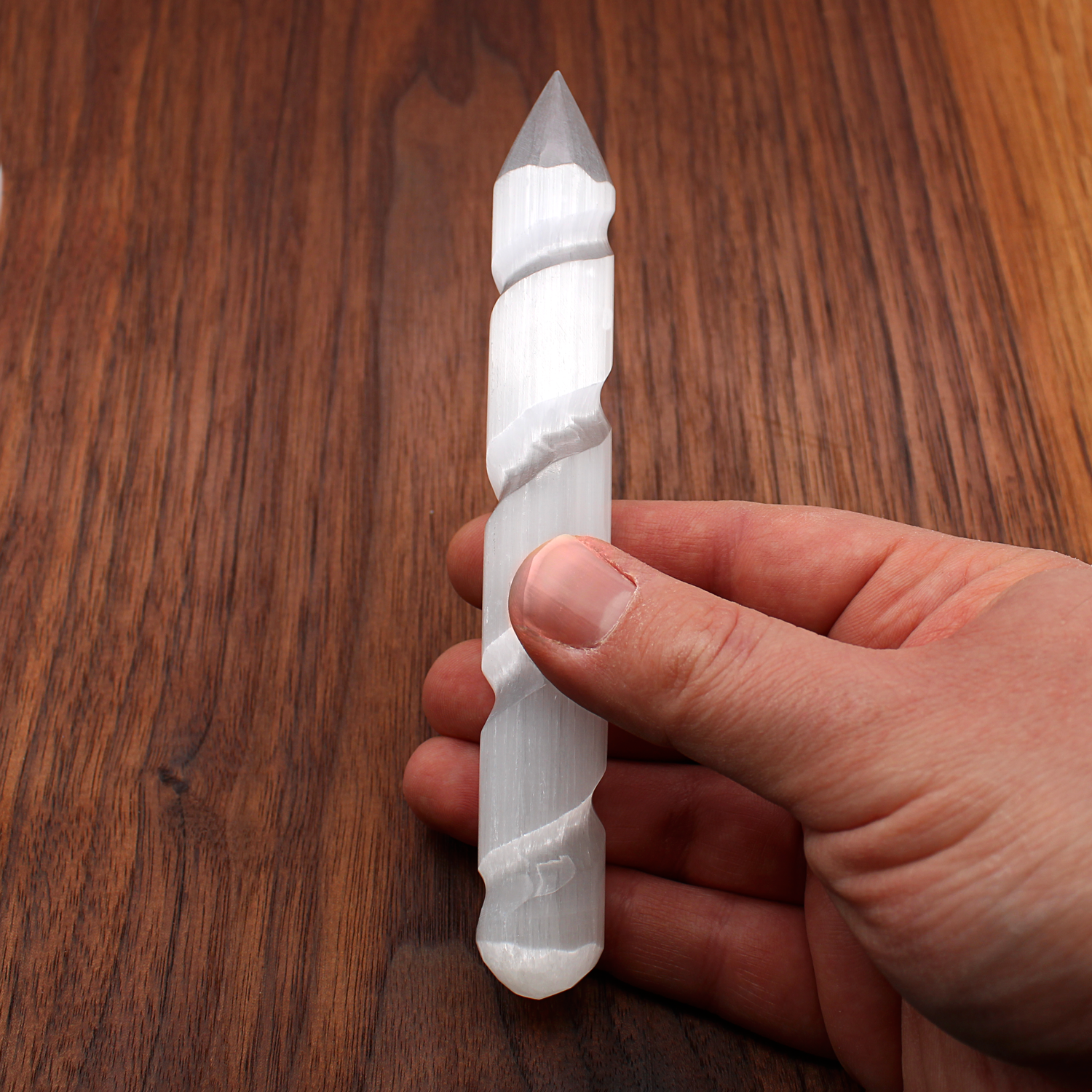 Hand holding a glowing Selenite spiral wand for directing energy and removing blockages.