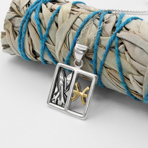 Horoscope pendant: Silver and gold Pisces necklace resting on a bundled sage smudge stick with blue string