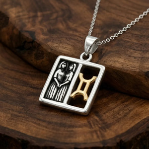 Gemini pendant zodiac jewelry, displaying a two-tone silver and gold horoscope design resting elegantly on a warm, dark wood grain surface