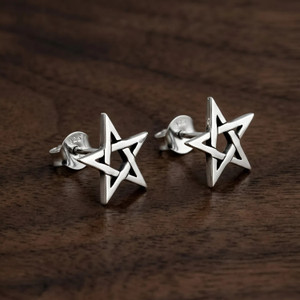 Star earrings designed as minimalist pentagram studs, resting elegantly on a warm, dark wood grain surface highlighting the polished silver finish