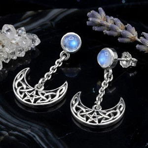 Crescent moon post earrings with rainbow moonstone accents, displayed on a dark surface alongside natural quartz crystals and lavender at our Wiccan store