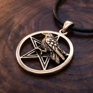 Gold crow pentagram necklace at our pagan jewelry store resting flat on a rich dark wood grain surface, highlighting the detailed feathers of the Wiccan raven familiar