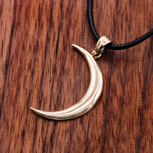 Witch moon pendant crafted in bronze at our pagan jewelry store, lying flat on a rich dark wood grain surface to emphasize its highly polished, glowing finish