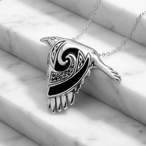Spirit animal Celtic raven pendant crafted in sterling silver with black spiral details, elegantly draped over white marble steps