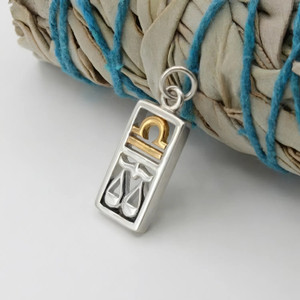 Libra necklace and zodiac charm in sterling silver and gold leaning against a white sage bundle at our witchcraft shop