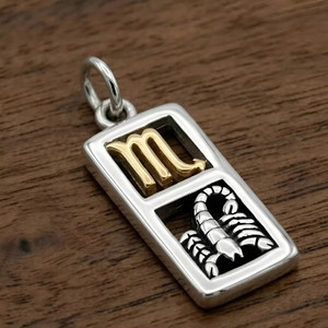 Scorpio pendant in .925 sterling silver and 14k gold vermeil resting on a dark wood background