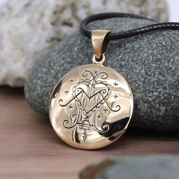 Ezili Freda Bronze Pendant with Black Cord Necklace Against a Rock Ezili Freda Bronze Pendant with Black Cord Necklace Against a Rock