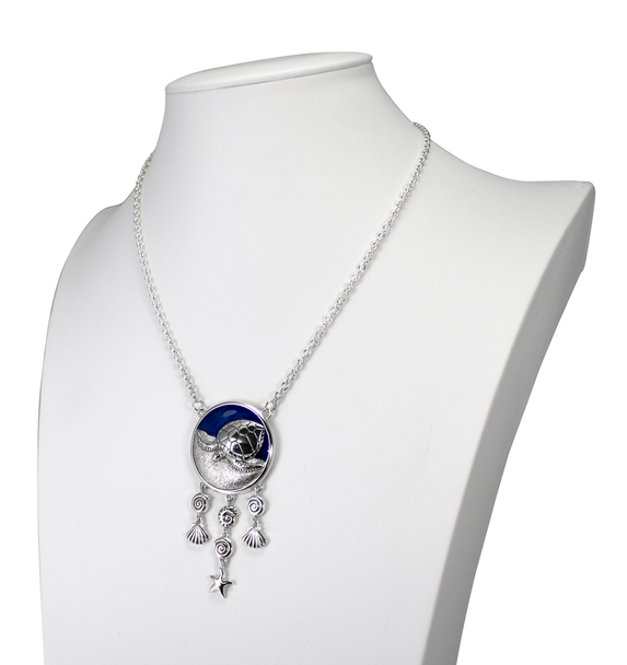 This large Sea Witch necklace features a turtle familiar animal against a vibrant blue enamel background, accented by dangling shells and five pointed star