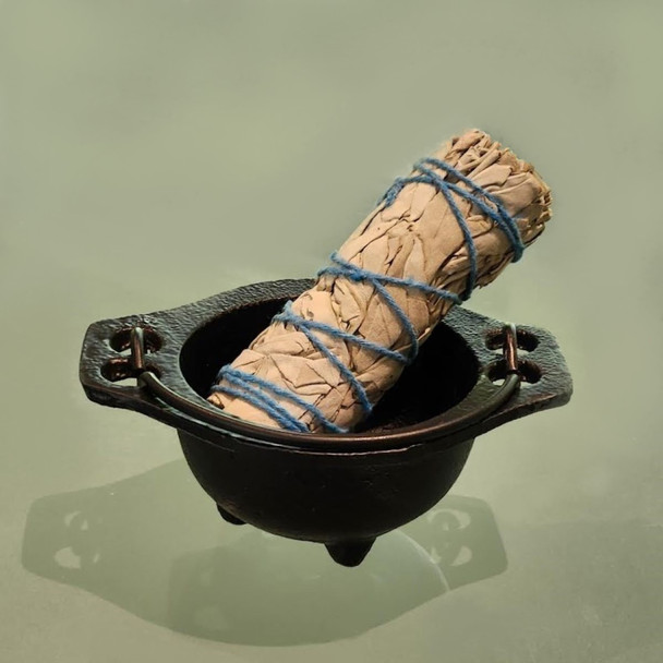 Baby cauldron, shown here as a smudging incense holder, with Witchcraft Essentials: White Sage Incense Smudging Wand (sold separately as part of our Apothecary Refill Witches baby cauldron sitting on seafoam green frosted glass with shadows.