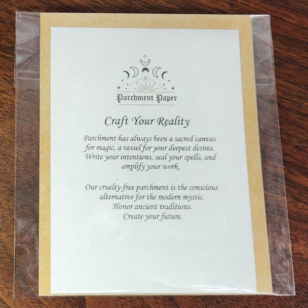 A product card for spell parchment paper is shown, sealed in a clear plastic sleeve on a dark wooden surface. The white card features a logo of moon phases and stars, with the title "Craft Your Reality." The text on the card describes the paper as a sacred canvas for magic and highlights its purpose as a cruelty-free, conscious alternative for the modern mystic, a key item among occult supplies.