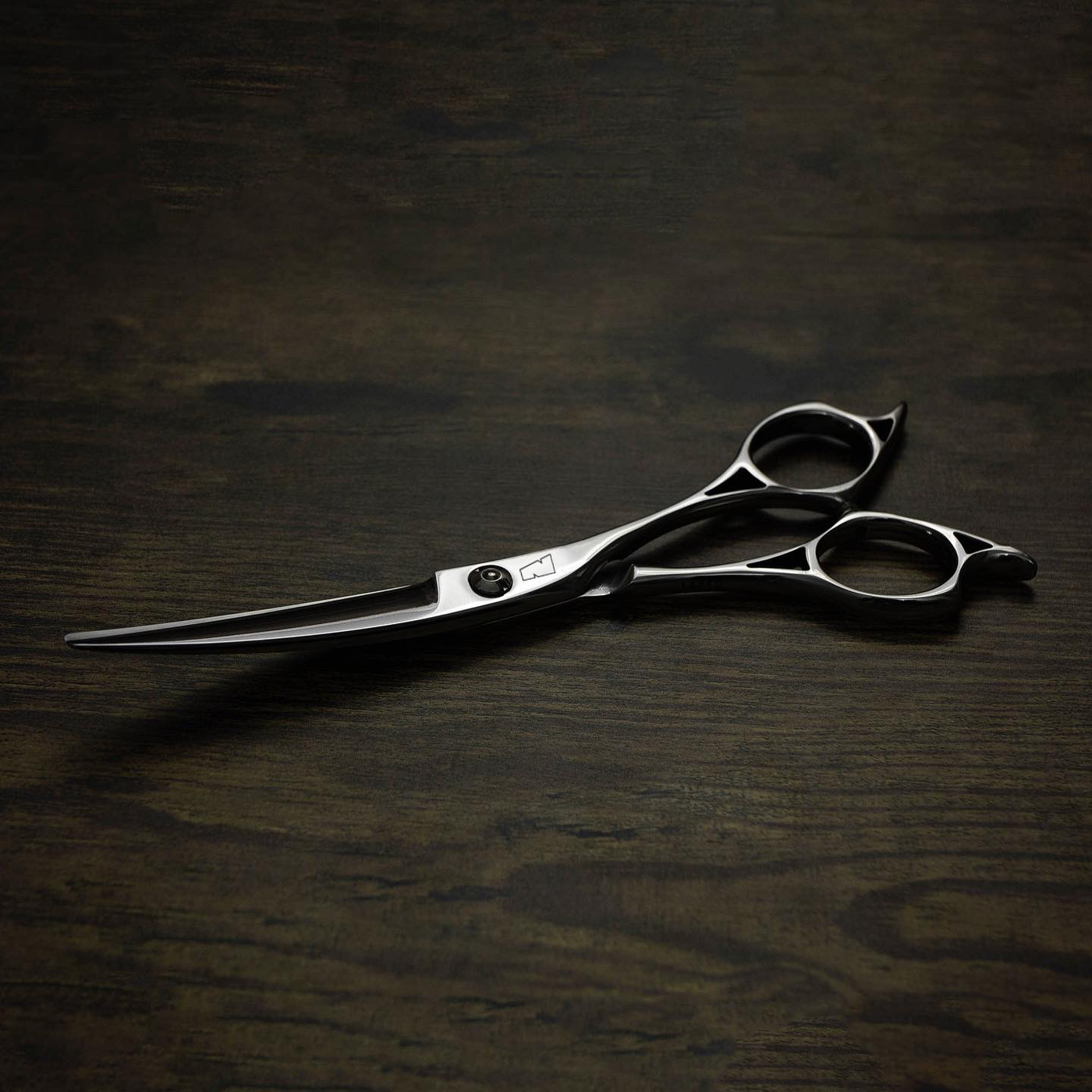 a silver right handed scissor with a black "N" logo laying flat on a dark background showing the blade curving upwards.
