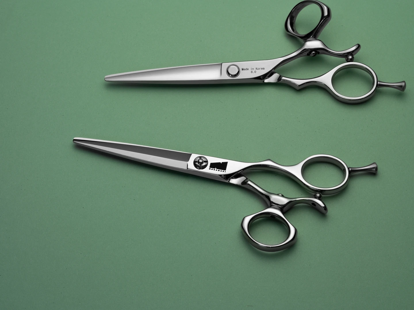 silver colored right handed hair scissor with black "N" logo and round swivel thumb ring on a green backgorund