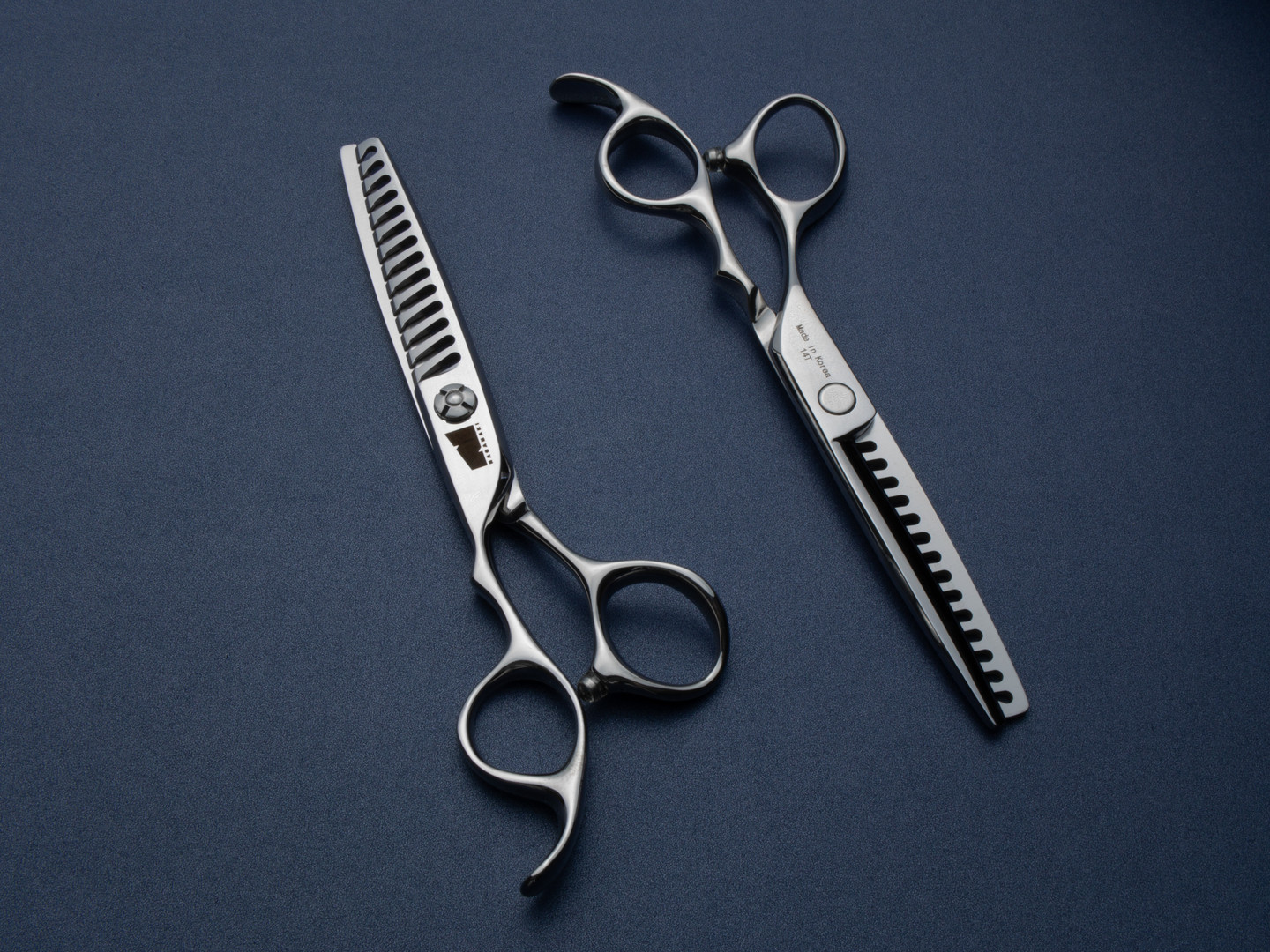 silver left handed scissors with black "N" logo and 14 teeth on one blade on a blue background