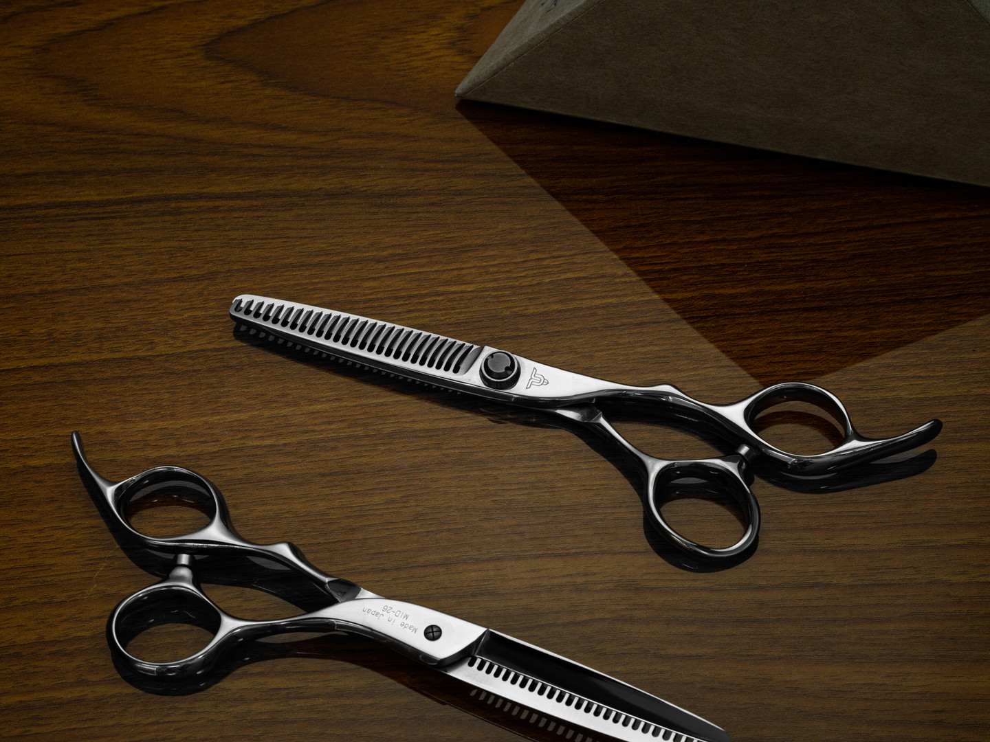 a silver right handed scissor with a "T' logo and 26 teeth on one blade against a brown background