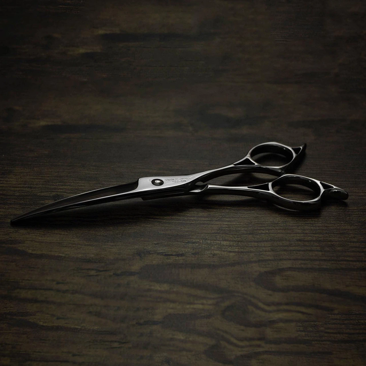a silver left handed scissor with a black "N" logo laying flat on a dark background showing the blade curving downwards