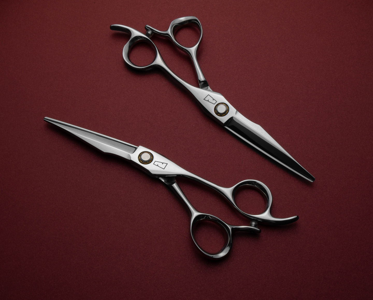 silver colored right handed hair scissor with black "N" logo and yellow ball bearing center against a red background