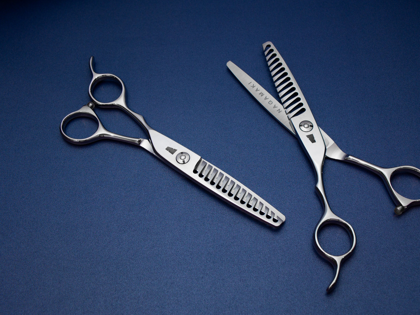 silver colored left handed hair scissor with black "N" logo with 14 teeth on one blade against a blue background