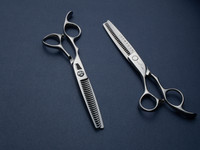 silver left handed scissors with black "N" logo and 25 teeth on one blade on a blue background