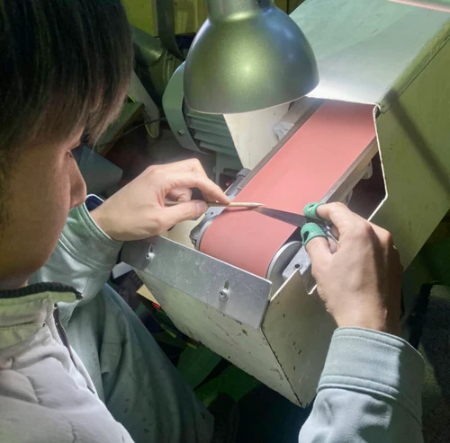 picture of man sharpening a scissors on a red belt grinder