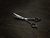 a silver right handed scissor with a black "N" logo laying flat on a dark background showing the blade curving upwards while slight opened