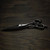 a silver left handed scissor with a black "N" logo laying flat on a dark background showing the blade curving downwards