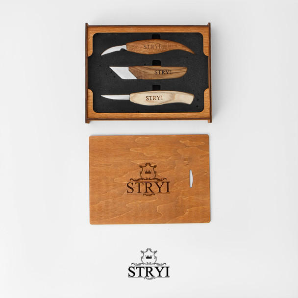 A photo of the Stryi 3 Piece Knife Set in Box with the wooden lid resting beside the box, and the three knives snuggled into the black foam that holds the knives in place.