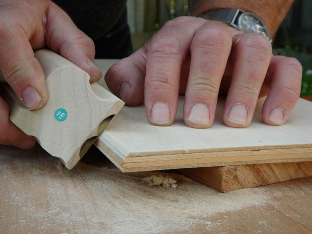 The carbide sanding block in use sanding the corner edge of a piece of wood.