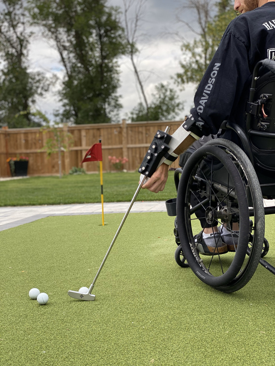 Person using adaptive Swing Mate equipment for golf. Front view of wheelchair, swing, and golf aid.

