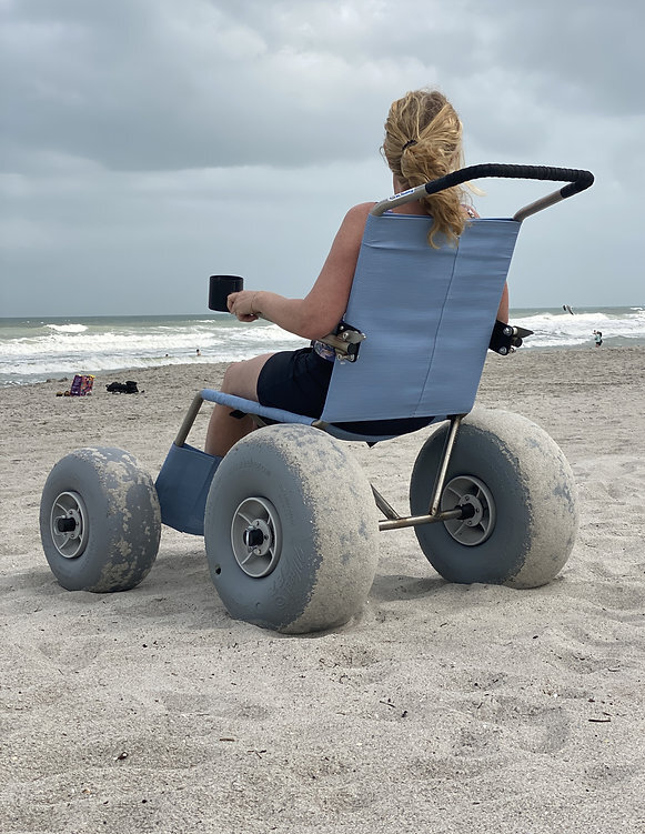 Rear view of the Beach Explorer wheelchair being pushed on sand.
