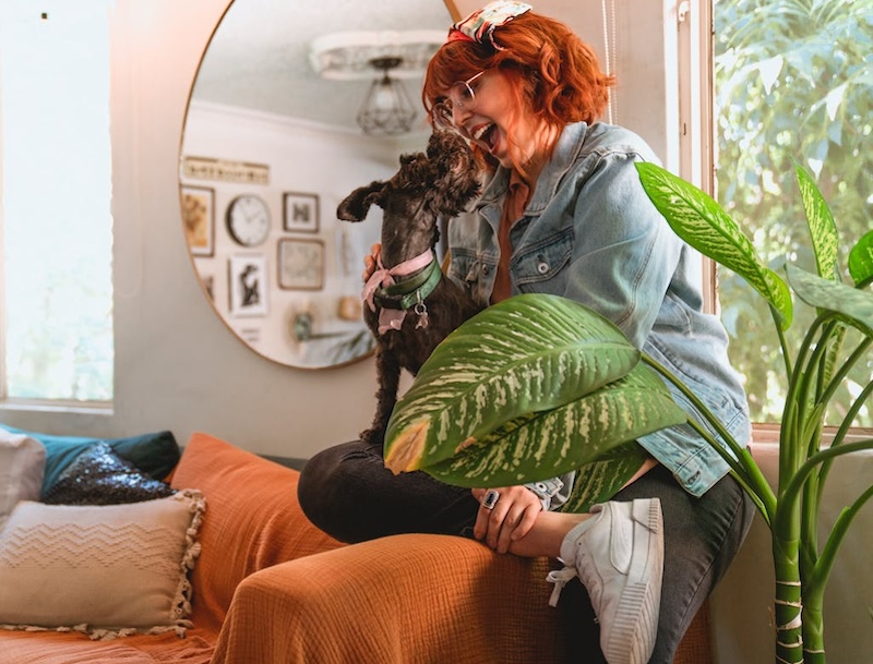 smiling-woman-petting-dog-next-to-potted-dieffenbachia-plant.jpg