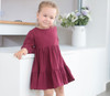 Generic Long Sleeve Linen Solid Colour Dress, A young girl wearing a long sleeve maroon linen dress with a tiered skirt, standing indoors near a white counter with a vase of flowers in the background.