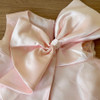 OONA Chloe Trapezold Dress, close-up of the dress showing a shiny, satin pink fabric with a large, elegant bow detail.