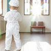 Minnie Me Liam Suspender Set, baby boy dressed in white suspender and pants set facing away indoors.