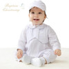 Minnie Me Bode Christening Romper Set, baby girl wearing a white christening romper with matching bonnet, sitting on a white surface.