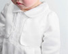 Minnie Me Jettson White Romper With Hat, close-up of a baby girl wearing a white romper with lace details and a matching hat, in a minimalist setting.
